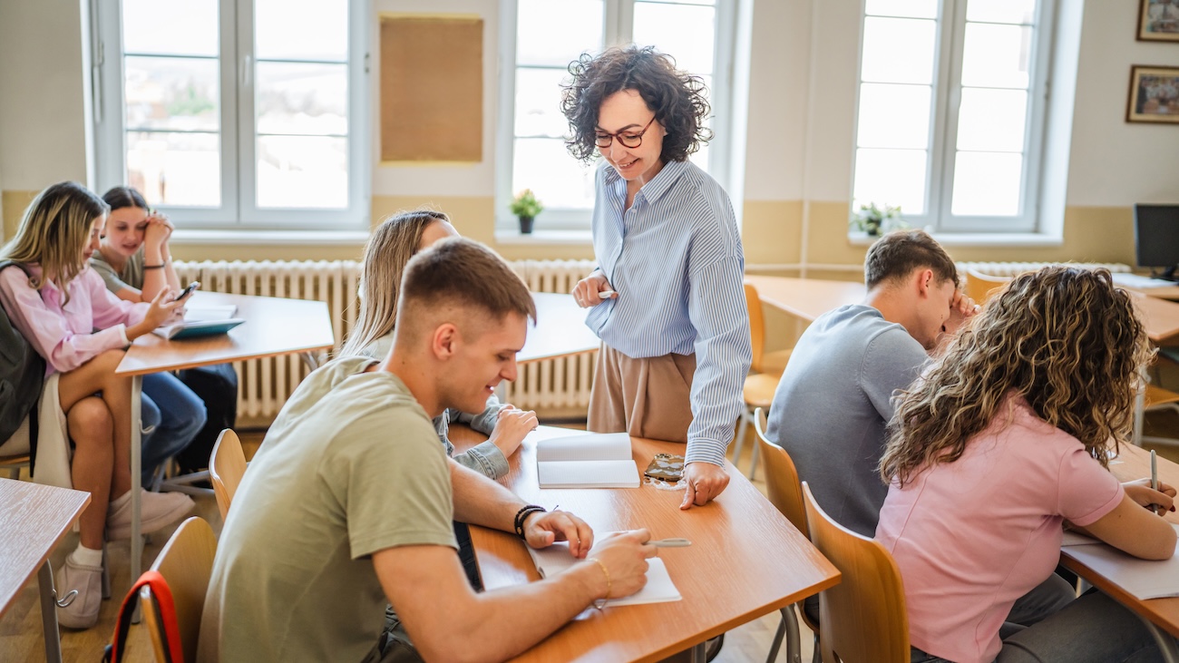 Female teacher talking with students in a high school classroom.